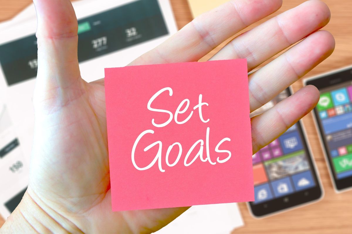 A hand holding a sticky note on which it says "set goals".