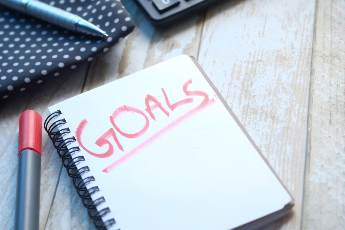 A notebook and a pen next to it with the word goals written inside.